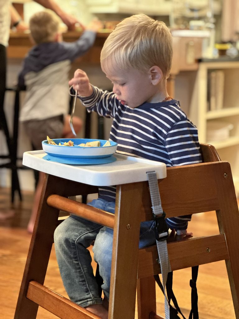 young boy eating with dine out tray on wooden high chair