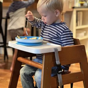 Young child eating with "dine out tray" on wooden high chair